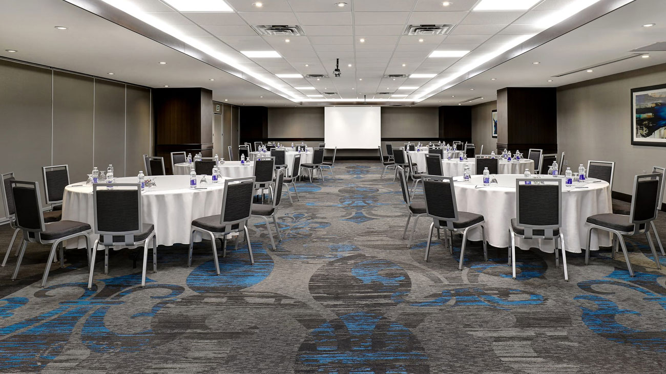 An expansive conference room equipped with multiple rows of chairs and a prominent projector screen for visual displays.